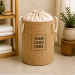 A cylindrical laundry hamper with rope handles, a fabric drawstring top and a front branding panel.