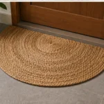 A semicircular jute mat with concentric braided rows and a straight edge for placement near a doorway.